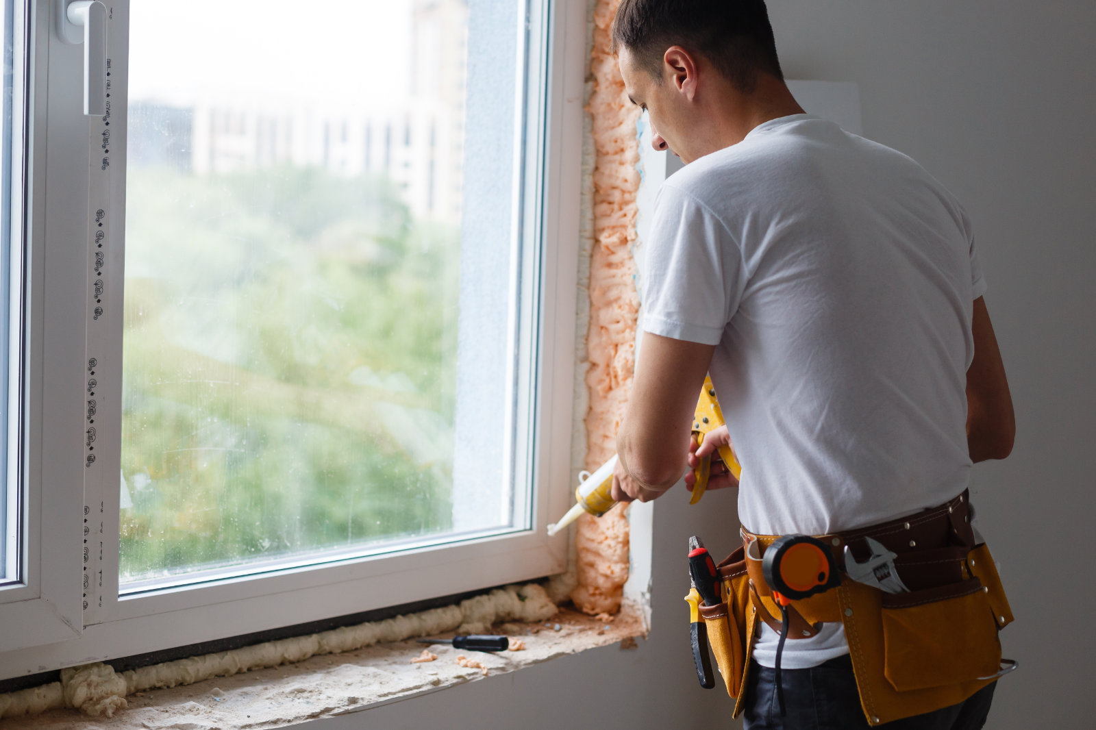 Caulking window with exposed insulation to seal air leaks.