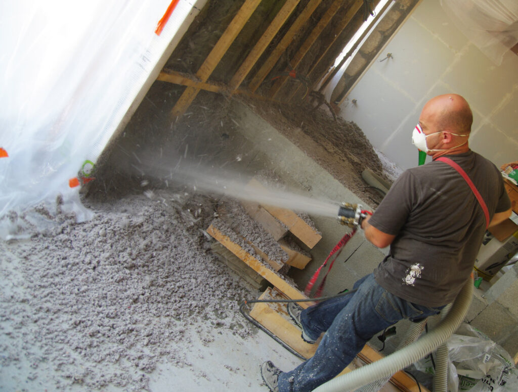 Insulation expert spraying cellulose into house wall.