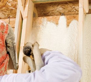 Worker spraying foam insulation in attic.