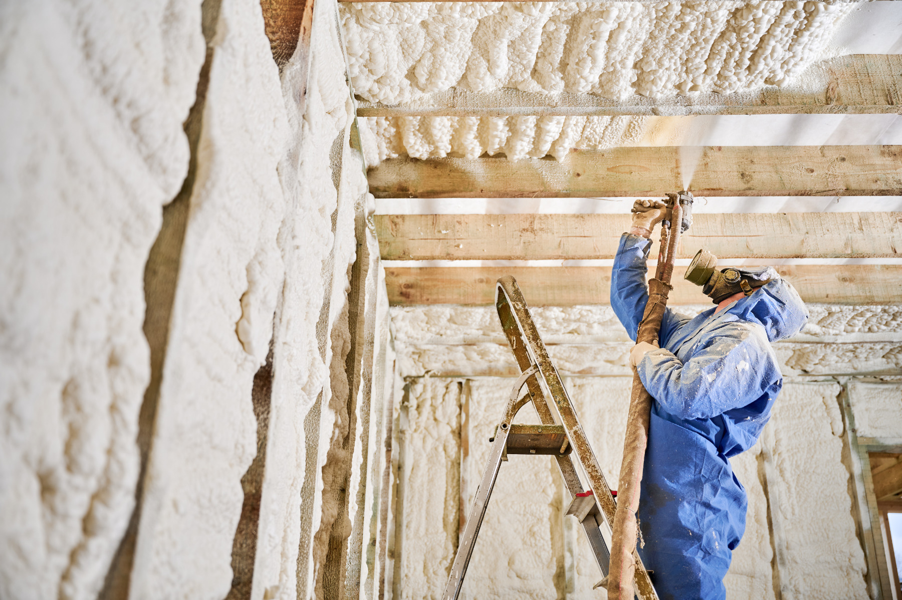 Contractor insulating ceiling beams and wall cavities with polyurethane foam spray. Residential building interior, airtight protection, renovation process and comfort concept.